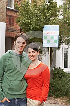 Couple In Front Of New Home With Sold Sign