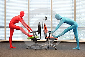 Couple in full body elastic suits exercising with chairs in office