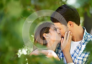 Couple, garden and kiss with love for date, bonding and romance with embrace in nature park. Man, woman and happy