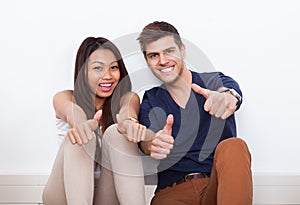 Couple gesturing thumbs up at home