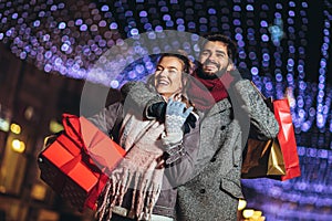 Couple with gift bag on Christmas lights background during walking in the city at evening