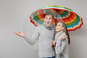 Couple girl guy in gray sweaters scarves together under umbrella isolated on grey wall background, studio portrait