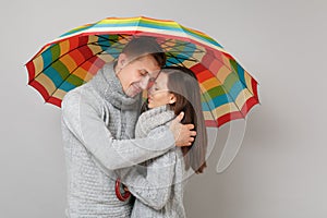 Couple girl guy in gray sweaters scarves together under umbrella isolated on grey wall background, studio portrait
