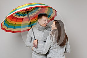 Couple girl guy in gray sweaters scarves together under umbrella isolated on grey wall background, studio portrait