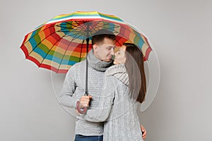 Couple girl guy in gray sweaters scarves together under umbrella isolated on grey wall background, studio portrait