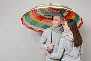 Couple girl guy in gray sweaters scarves together under umbrella isolated on grey wall background, studio portrait