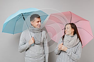 Couple girl guy in gray sweaters scarves together under umbrella isolated on grey wall background, studio portrait