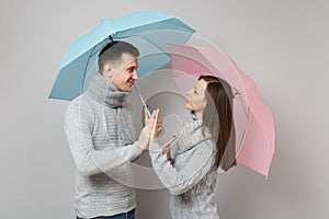 Couple girl guy in gray sweaters scarves together under umbrella isolated on grey wall background, studio portrait