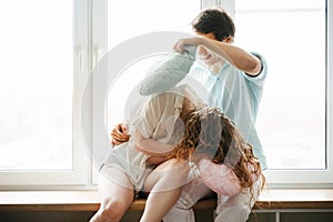 Couple girl and guy play with pillows near window.
