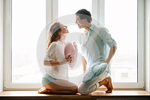 Couple girl and guy play with pillows near window.