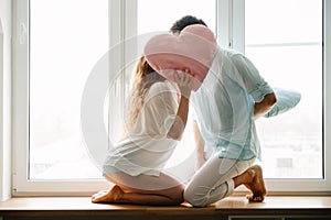 Couple girl and guy play with pillows near window. photo