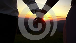 Couple is giving hand to each other at the background of the colourful sky during the sunset. Close-up view of the