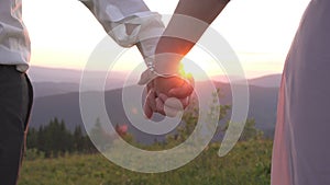 Couple giving hand to each other. Close-up view of the couple holding hands in the sunset. Romantic outdoor view.