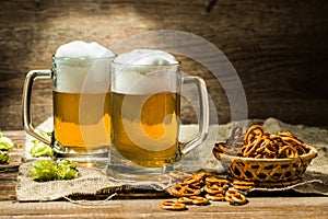 Couple glasses of beer froth with hop and pretzels