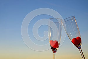 Couple glasses of champagne with red marmalade hearts on blue sky background with copy space, selective focus