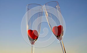 Couple glasses of champagne with red marmalade hearts on blue sky background, selective focus