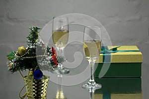 A couple of glasses with gold champagne on a white wooden table with Christmas balls with a sprig of spruce on the red background.