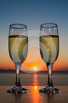 Couple of glasses of wine at sunset on the table, closeup, sun between glasses