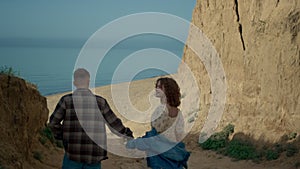 Couple going down coast to sandy beach. Happy woman adoringly looking at man.