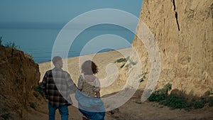 Couple going down coast to sandy beach. Happy woman adoringly looking at man.