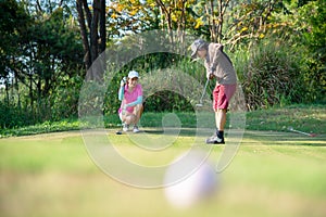 Couple golf player putting golf ball on the green golf.  Asia man and woman putting golf ball on tee with club in golf cour