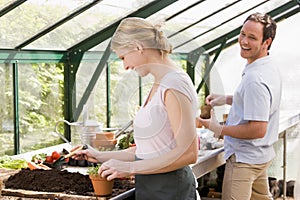 Couple in greenhouse putting soil in pots smiling