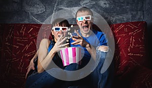 A couple of guy and girl watch a scary movie in 3D glasses and scream with fright. Popcorn.
