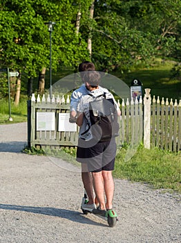 A couple of guys ride an electric scooter in the park. View from the back