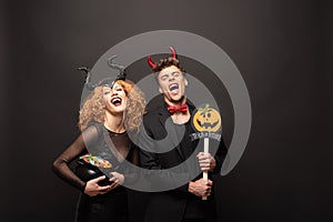 Couple in halloween costumes holding pot with candies and pumpkin trick or treat sign on black