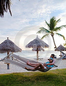 Couple in a hammock at Palm Beach Aruba Caribbean, white long sandy beach with palm trees Antilles