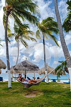 Couple in a hammock at Palm Beach Aruba Caribbean, white long sandy beach with palm trees Antilles