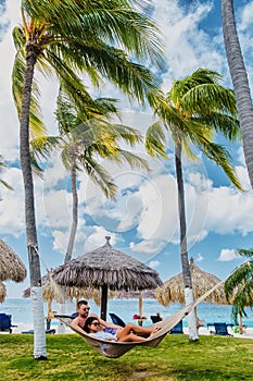 Couple in a hammock at Palm Beach Aruba Caribbean, white long sandy beach with palm trees Antilles