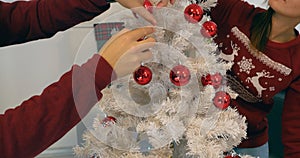 Couple hands decorating white Christmass tree