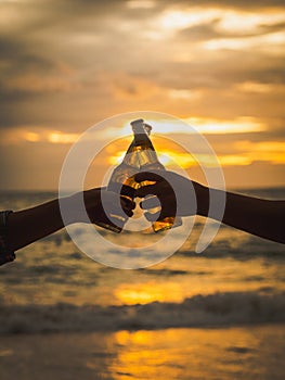 Couple hands holding beer bottles and clanging on the sunset beach. Party, Holiday, Summer, Friendship Concept.