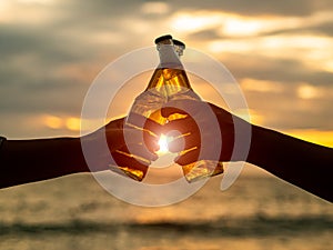 Couple hands holding beer bottles and clanging on the sunset beach. Party, Holiday, Summer, Friendship Concept.