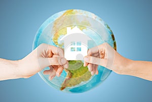 Couple hands holding green house over earth globe