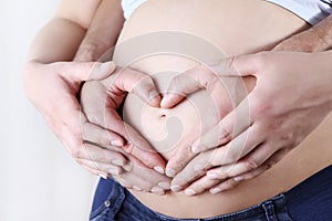 Couple hands making a heart shape on the pregnant belly