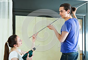 Couple hanging curtains at window