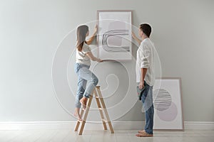 Couple hanging picture on wall together in room. Interior design