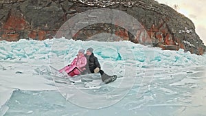 Couple has fun during winter walk against background of ice of frozen lake. Lovers lie on clear ice, have fun, kiss and