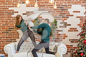Couple have fun and do pillow fight in room. Christmas decor. Concept of family and Christmas