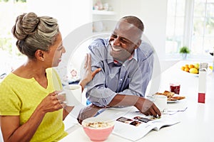 Couple Having Breakfast And Reading Magazine In Kitchen