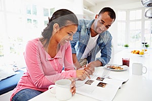 Couple Having Breakfast And Reading Magazine In Kitchen