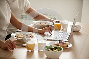 Couple having breakfast using laptop on dining table, close up