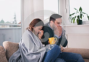 Couple having flu and sitting on sofa covered with blanket
