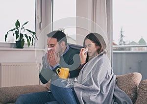 Couple having flu and sitting on sofa covered with blanket
