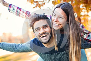 Couple having fun man giving piggyback to woman in park