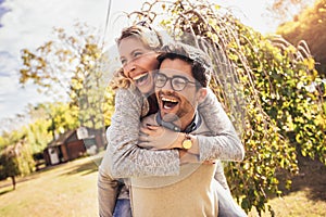 Couple having fun man giving piggyback to woman in park