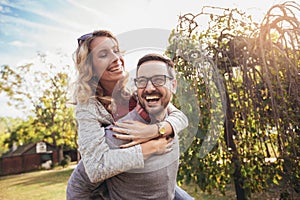 Couple having fun man giving piggyback to woman in park