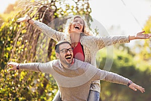 Couple having fun man giving piggyback to woman in park